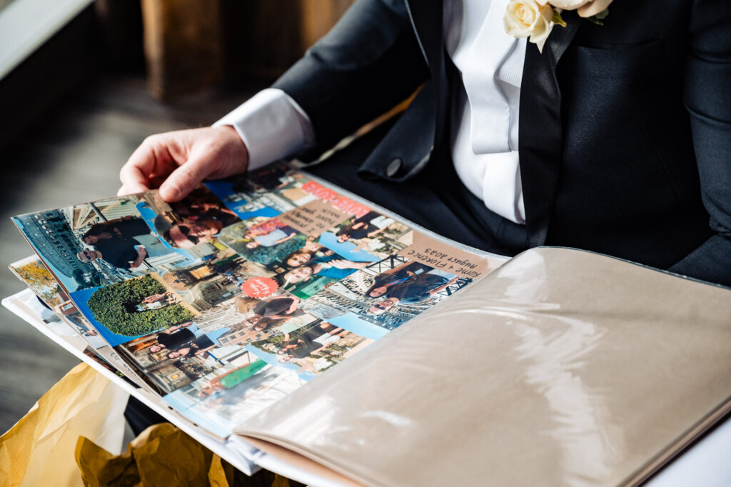 Close-up of the groom looking through a colorful scrapbook, seated near a window with golden light.