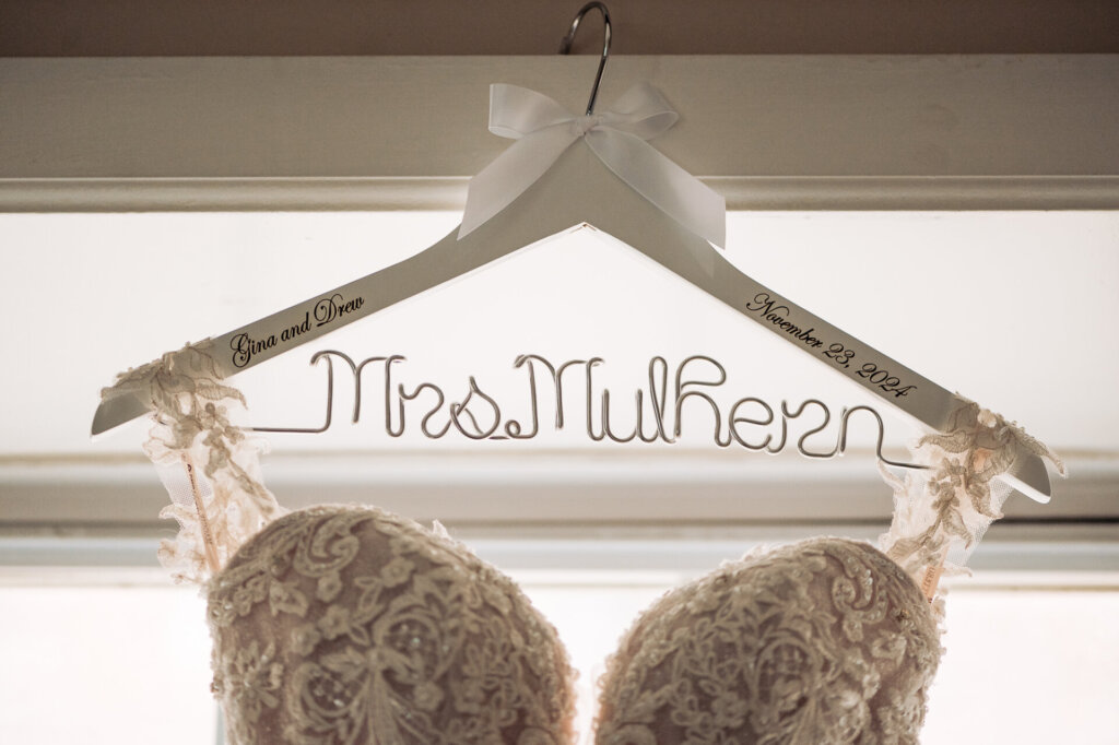 Detail shot of the dress on a hanger engraved with 'Mrs. Mulhern,' capturing the lace neckline and personalized hanger.