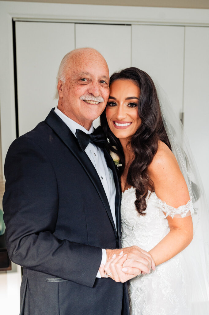 Bride standing with her father in a heartfelt moment, as he looks at her with pride and joy, both smiling warmly