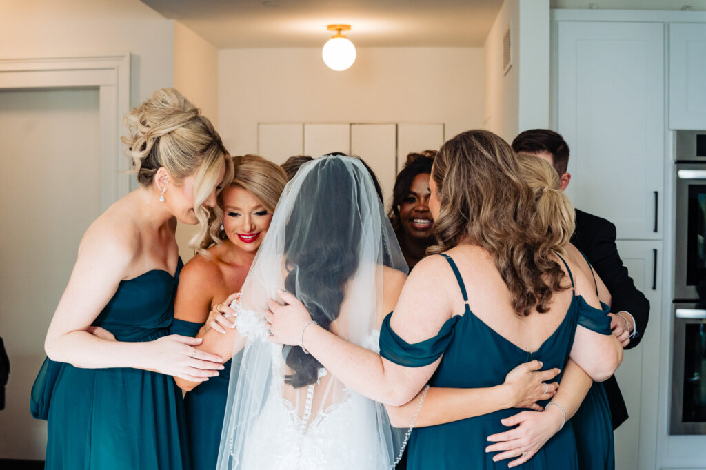 Bridal party gathering in a circle, holding hands with the bride as they bow their heads in a heartfelt moment