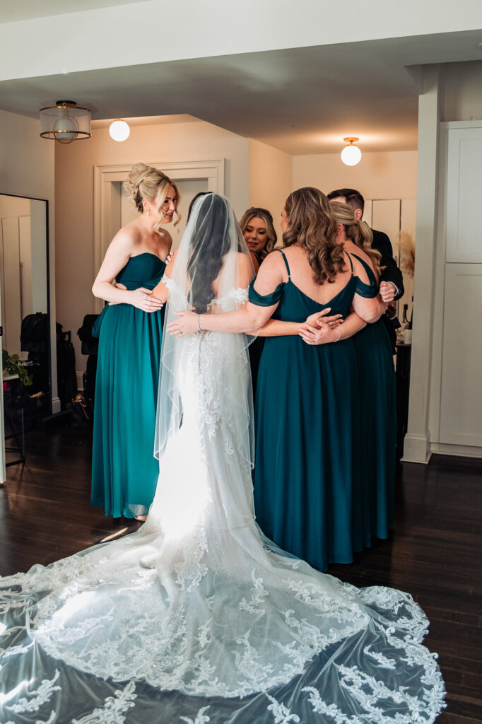 Bride standing with her bridal party, dressed in emerald green gowns, as they share an emotional and supportive moment before the wedding.