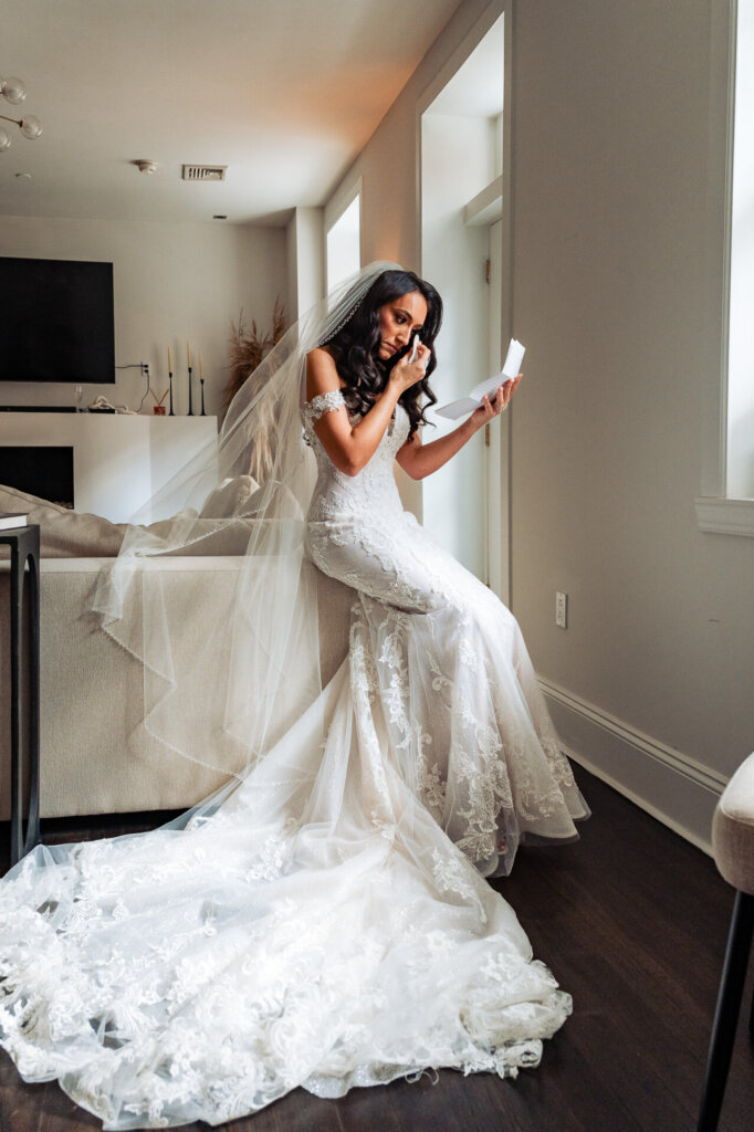 Bride sitting in a bright living room, reading a personal letter, her wedding gown and veil elegantly draped around her