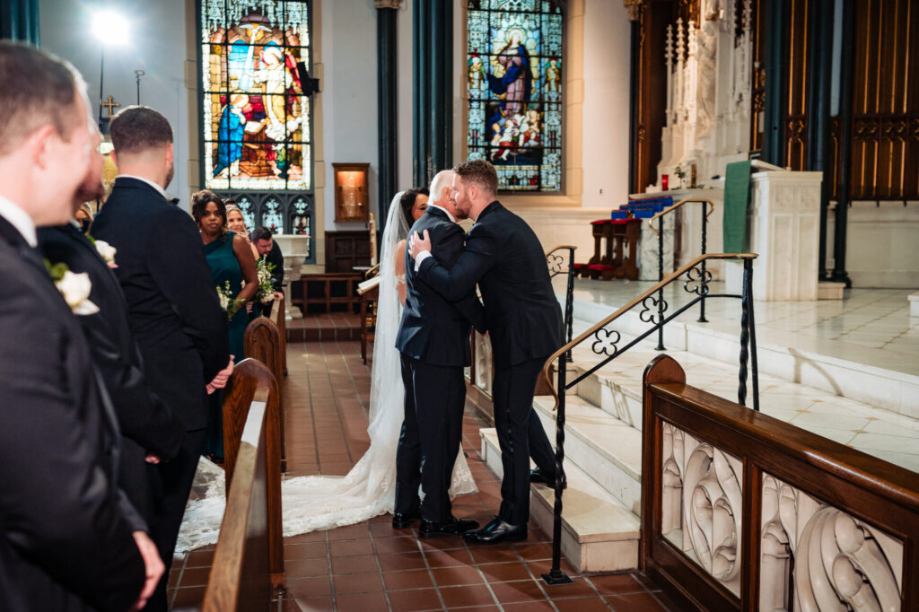 Groom hugging a family member as guests in the pews watch warmly during the wedding ceremony
