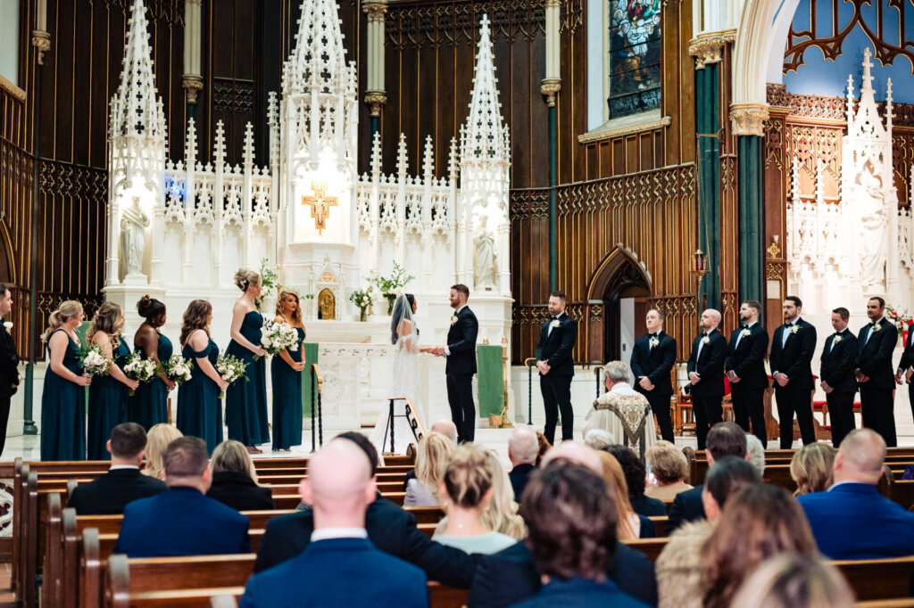 Bride and groom standing together at the altar, surrounded by their bridal party, as the officiant presides over the ceremony.