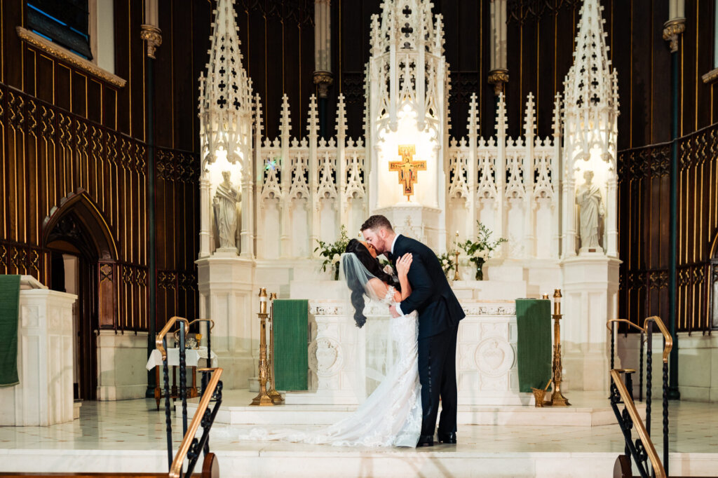 Bride and groom sharing their first kiss at the altar, framed by the intricate details of the cathedral’s ornate backdrop.