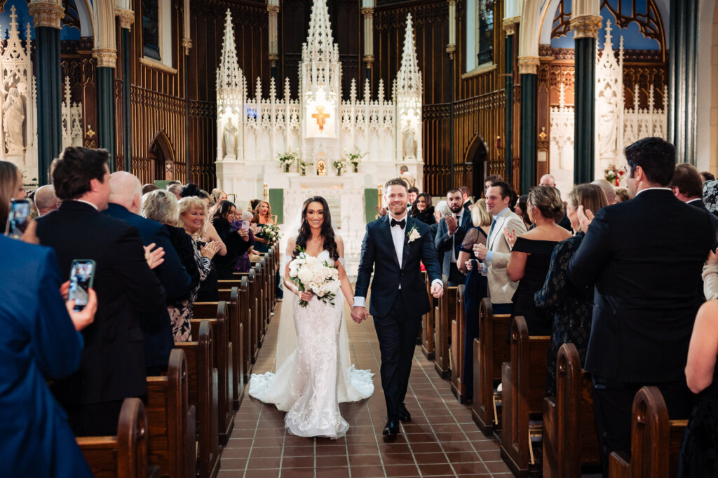 Bride and groom walking joyfully down the aisle as newlyweds, holding hands and smiling, surrounded by cheering guests.