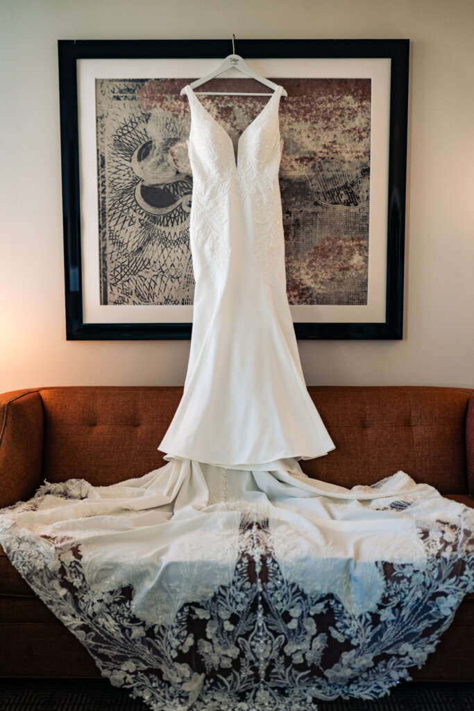 A white lace wedding gown draped over a sofa, with its long train cascading onto the cushions.