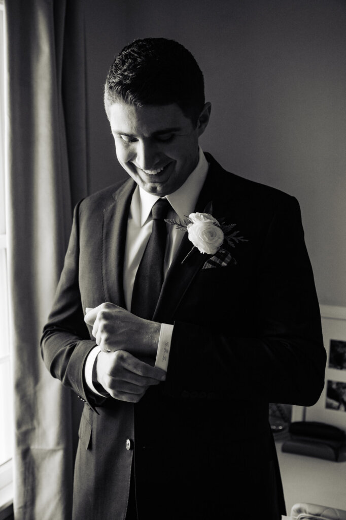 A candid moment capturing the groom adjusting his jacket, smiling as he prepares for the big day.