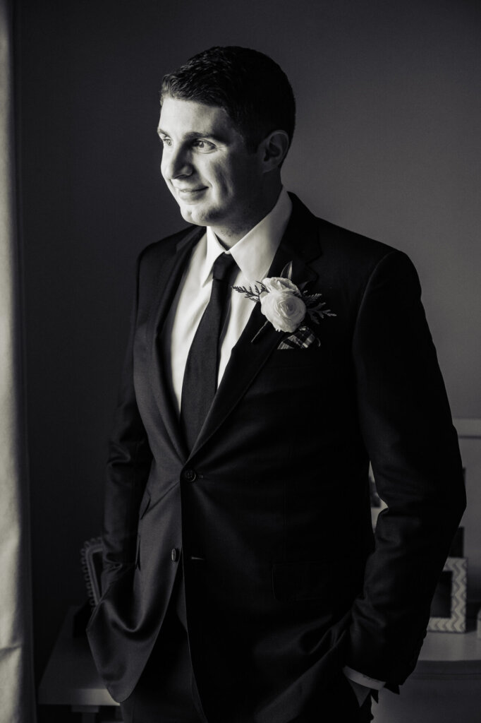 A classic groom portrait in black and white, highlighting his sharp tuxedo and elegant boutonniere.
