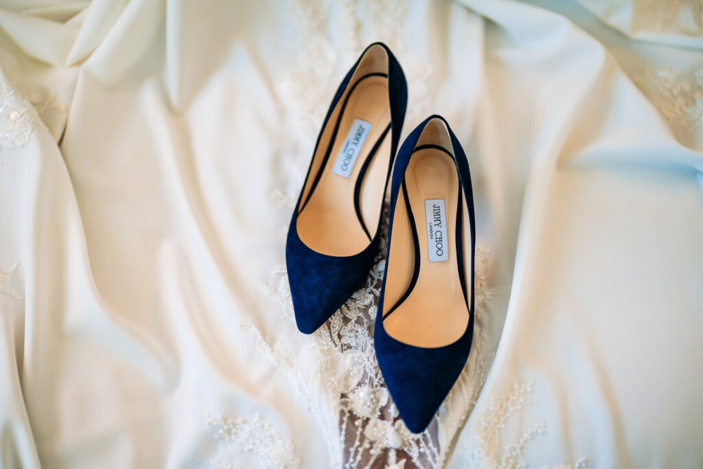 A pair of deep blue pointed-toe wedding heels set on a soft, ivory bridal robe.