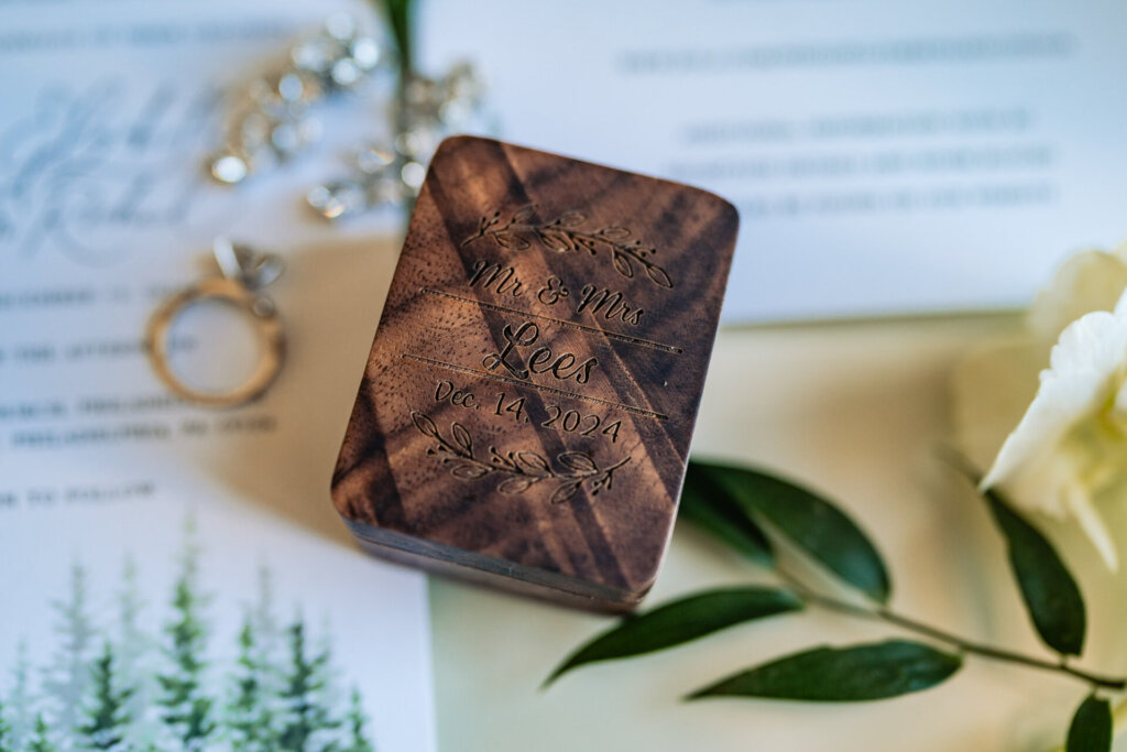 A detailed shot of wedding rings placed on top of a personalized wooden ring box, surrounded by floral accents.