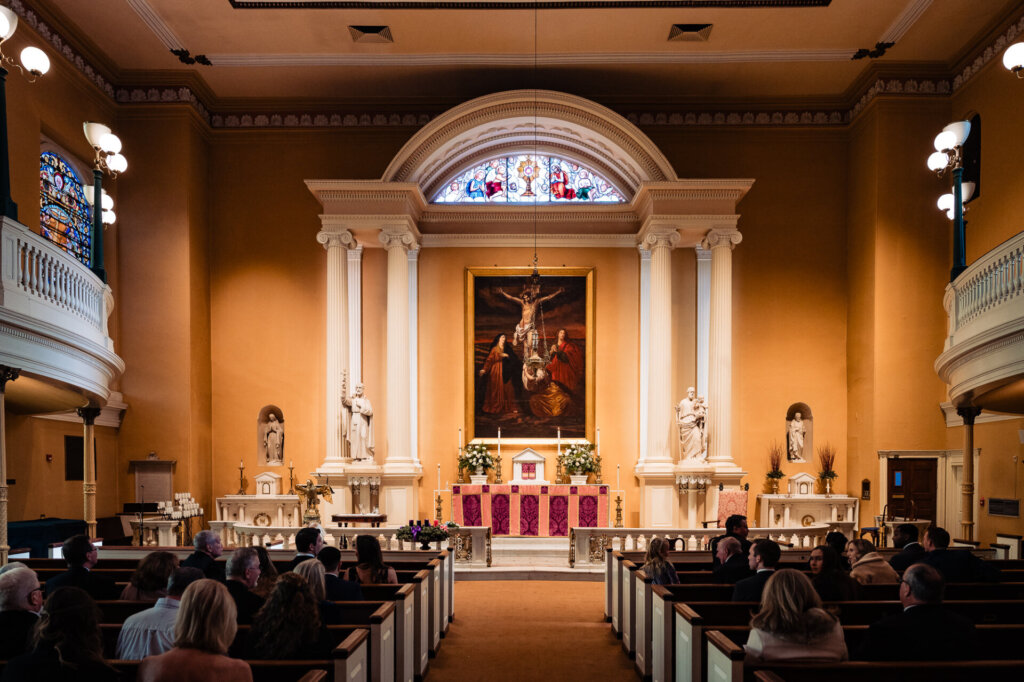 A wide-angle shot of a beautifully decorated church with tall white columns, stained glass windows, and a golden-hued altar.