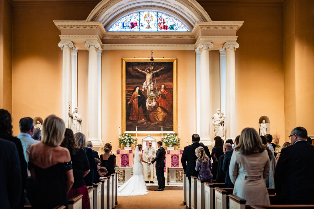 A heartfelt moment as the couple stands before the priest in an elegant church setting.