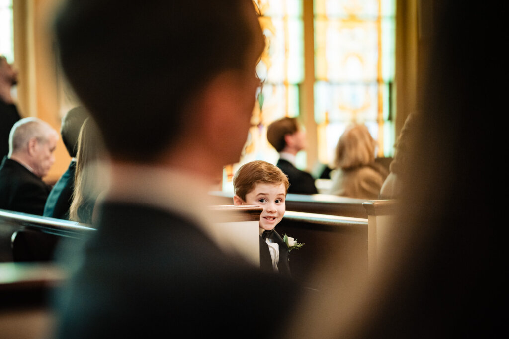 A candid shot of a little boy dressed in a suit, watching the ceremony through the blurred foreground.