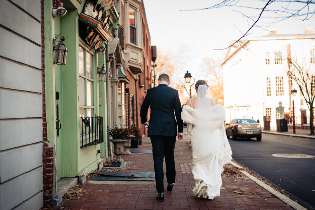 The couple strolls hand in hand through a charming, historic neighborhood, the bride’s veil flowing behind her.