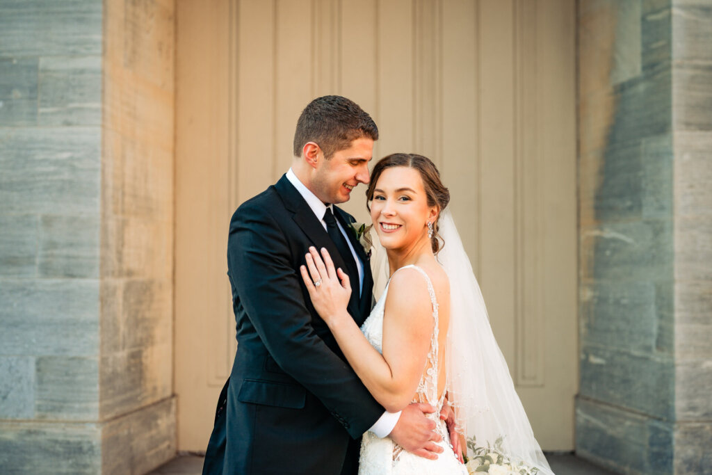 A warm and intimate moment as the groom holds his bride close, both smiling in the golden afternoon light.