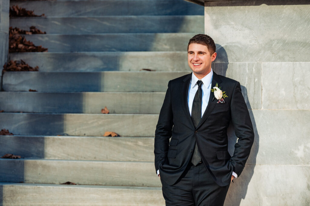 A sharp portrait of the groom, hands in pockets, standing confidently against a grand outdoor staircase.