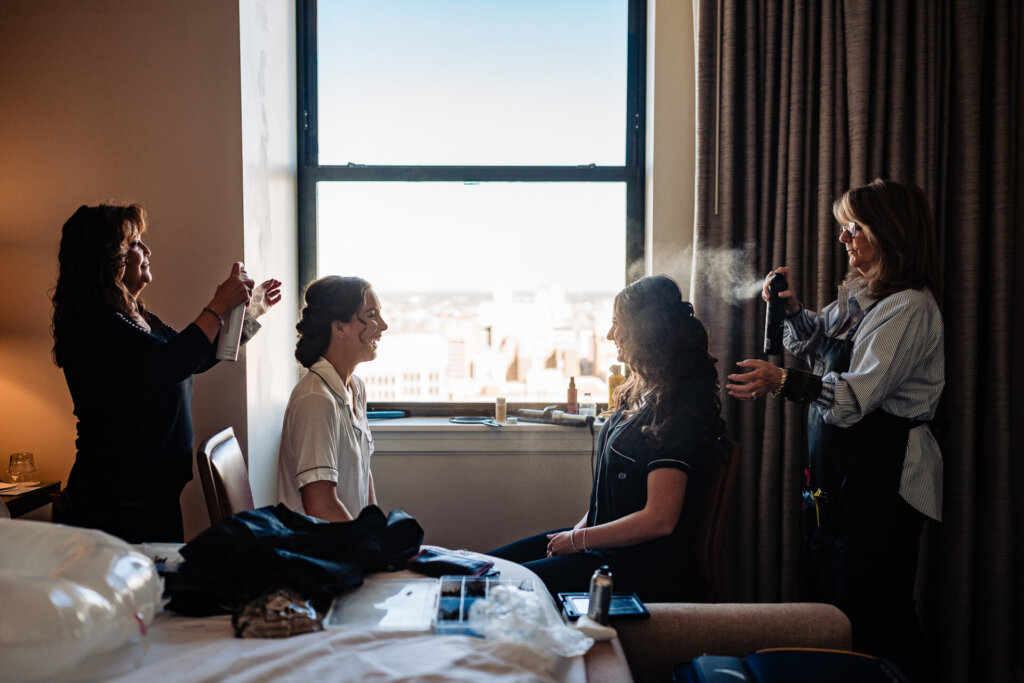 A candid moment of the bridal party helping the bride get ready near a bright window.