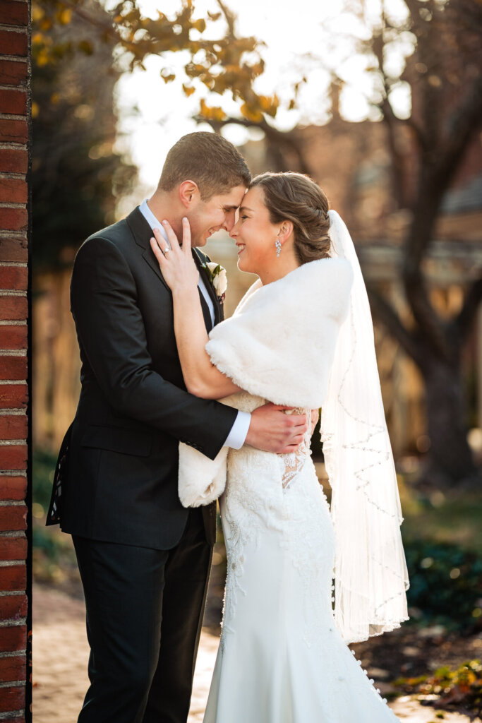 A warm embrace as the groom holds his bride close, with golden light filtering through the trees.