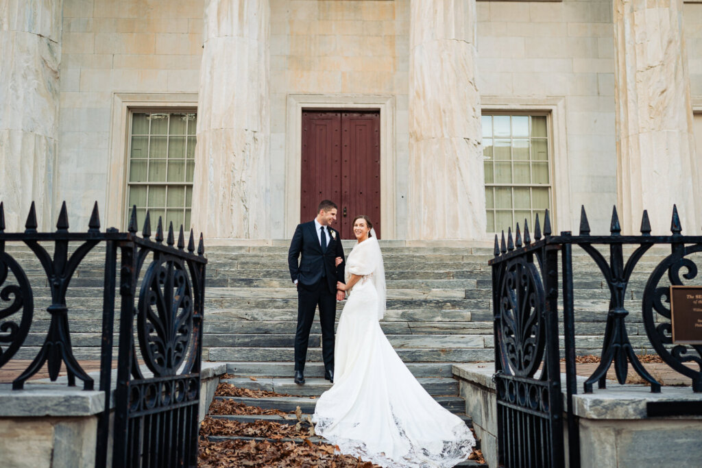A dramatic image of the couple descending grand stairs, framed by elegant black iron railings.