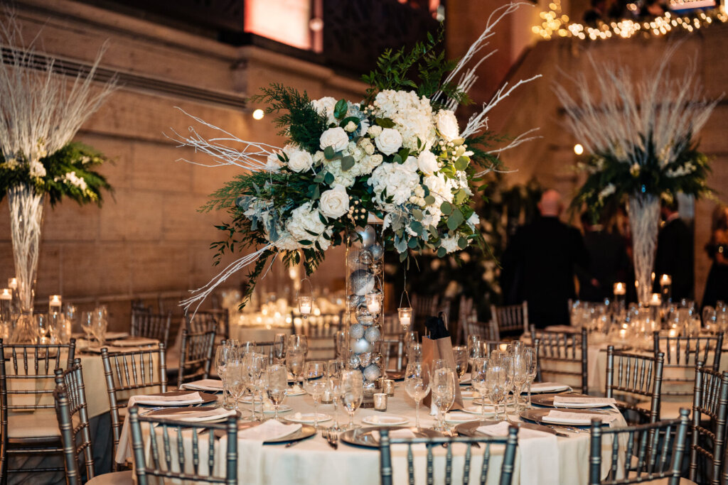 A stunning venue with high ceilings, warm lighting, and tall floral arrangements on round tables.