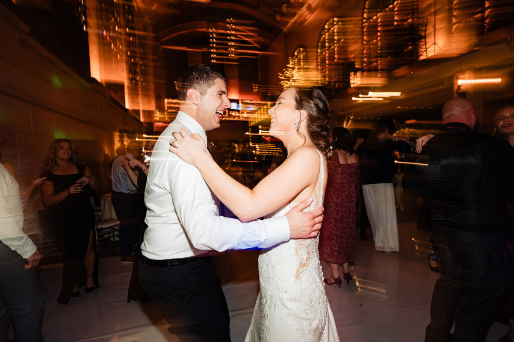 A fun and dynamic shot of the couple enjoying the dance floor with warm golden lighting.